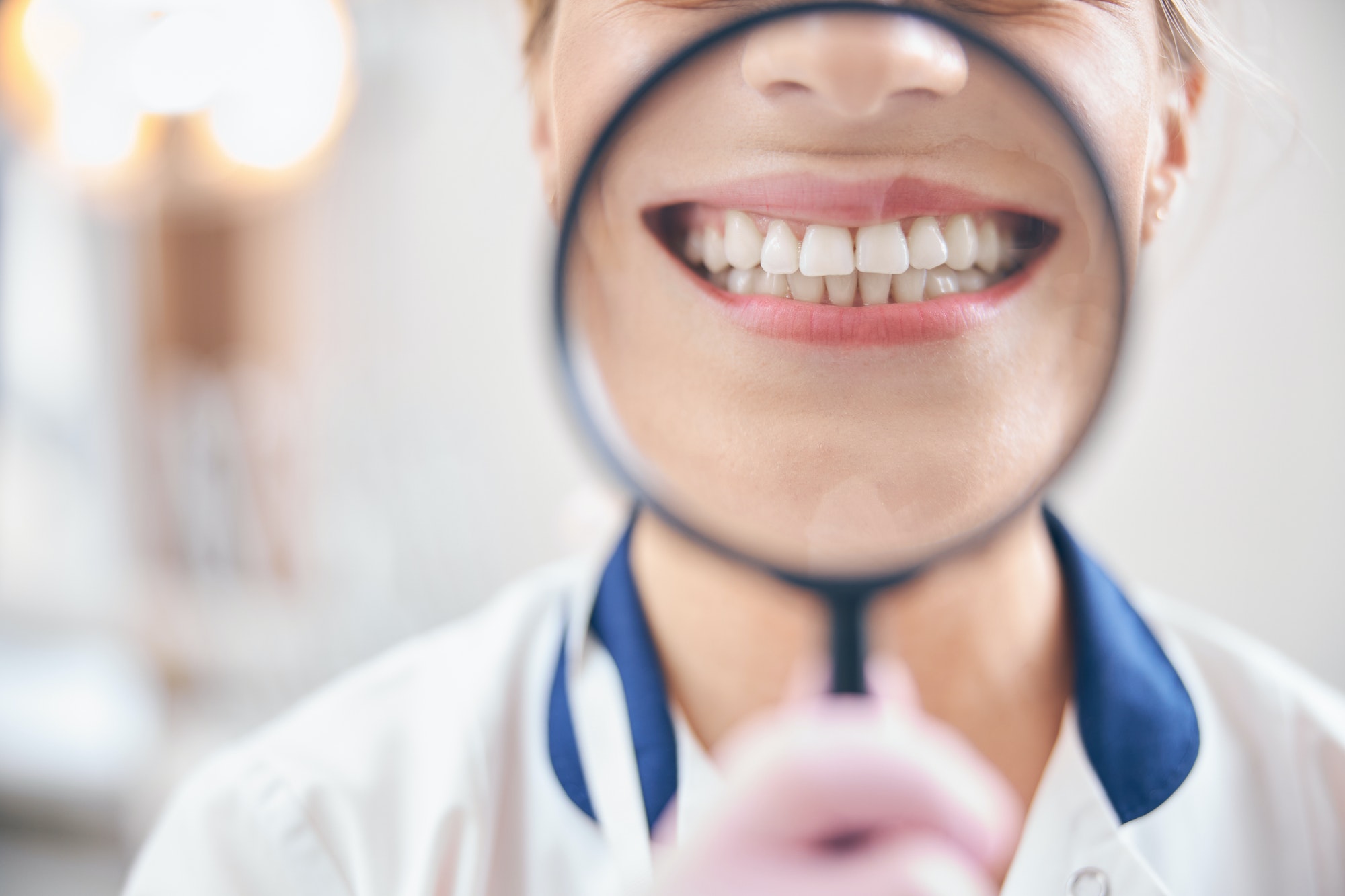 Joyful female dentist smiling through magnifier in office